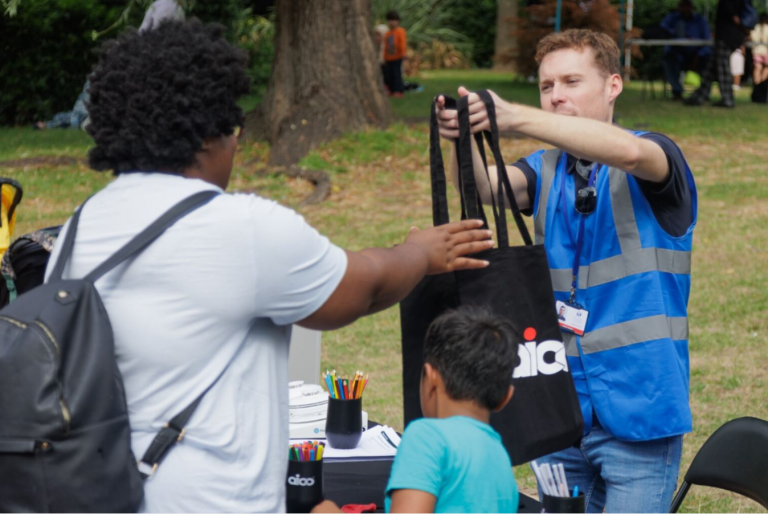 young white male with blue high vis vest passing black canvas tote to young asian boy