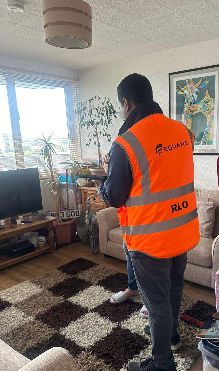 Male in high vis jacket holding clipboard standing in a living room