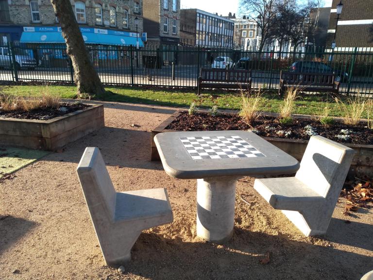 Two stone chairs arranged around a stone table with a chess board inlaid on the top, standing in the middle of Athlone Gardens