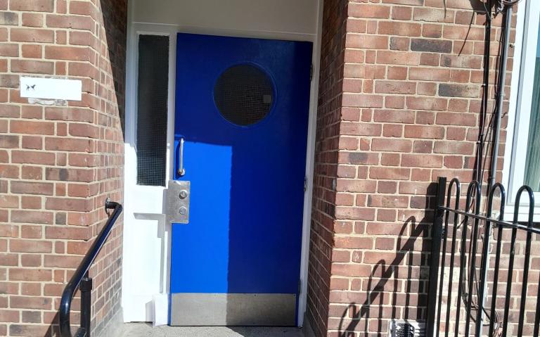 blue door with round window connected to red brick building with new silver fob entry