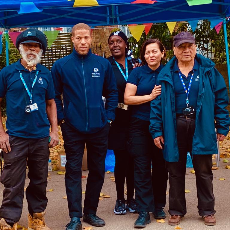 Picture of three men and two women dressed in caretaker uniform outside a gazebo with bunting