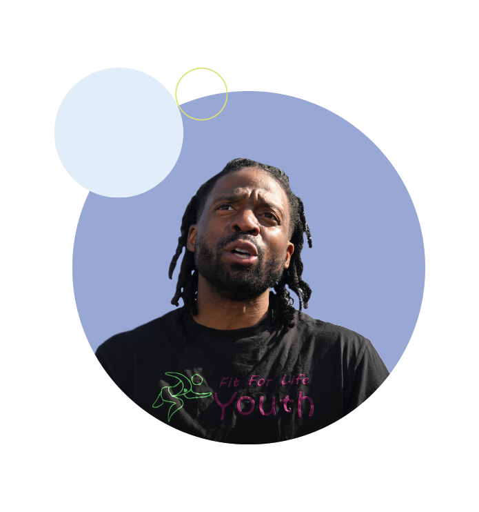Person wearing a “Fit For Life Youth” T-shirt standing outdoors against a blue graphic background