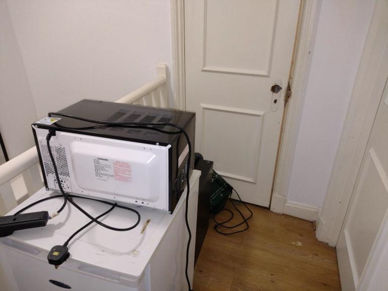 A fridge, microwave and vacuum cleaner block a communal means of escape, along with a damaged fire door.