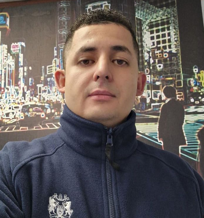 I mage of white man with brown eyes and dark hair looking into the camera wearing a navy blue fleece with the Council logo on it