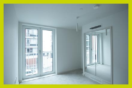A bare white bedroom showing a built in mirror and full length windows