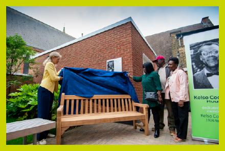 A councillor and Kelso Cochrane family unveil a bench beside a poster of Kelso Cochrane