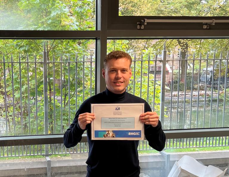 Young, white male,in dark jumper, holding apprenticeship certificate