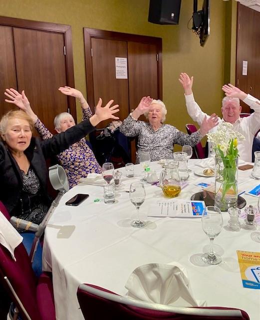 four people wave their arms in the air at a lunch event