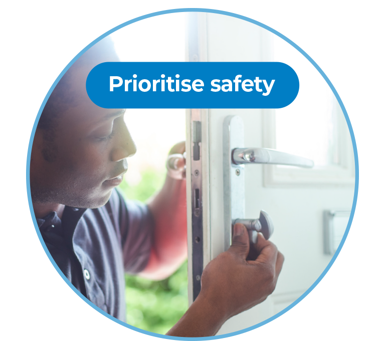 A graphic of a large circle with a photo inside. The circle has a light blue border. The photo is of a person fitting the lock of a front door to a house. This photo is the background of the graphic. On top of top of the photo is the words “Prioritise safety” in white text on a blue background.