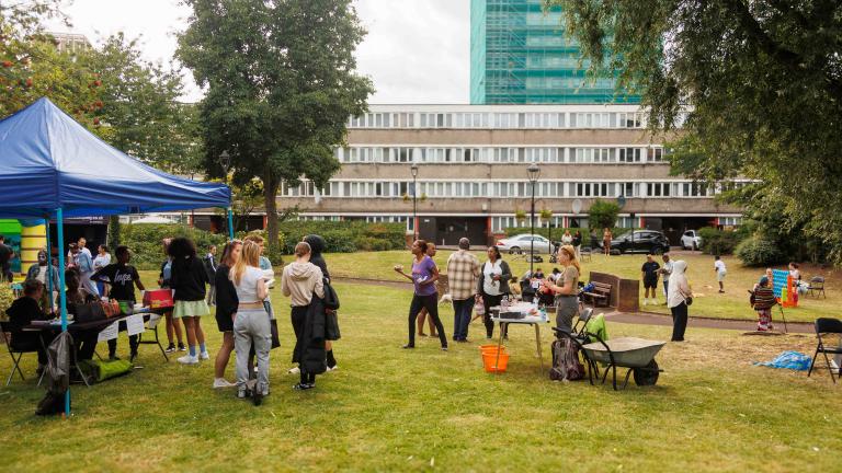 a number of people standing on a green with tall buildings in the back grround and stalls in the foreground