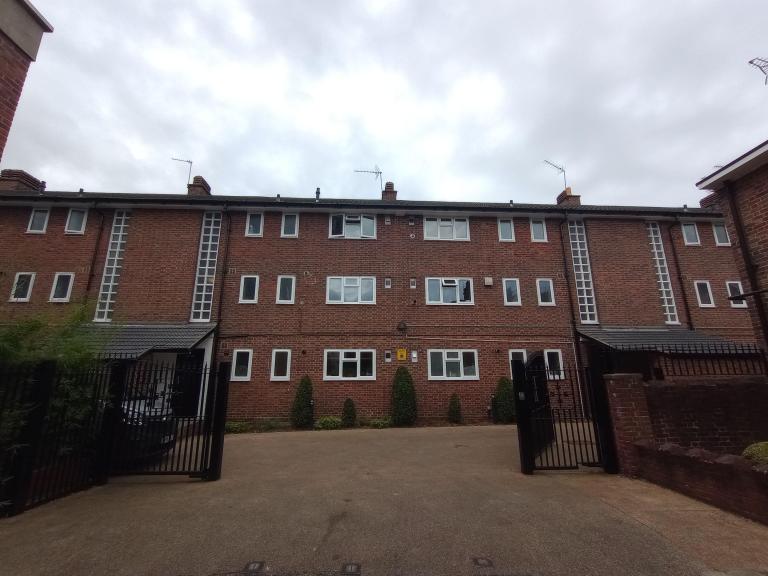 image of The Sandhills building - red brick and new white double glazed windows with black iron gate in the foreground