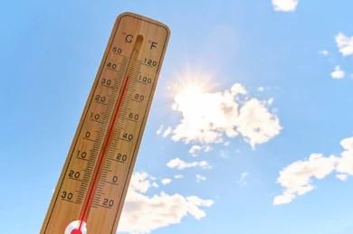 plastic thermometer held up infront of a blue sky with sunshine and few clouds 