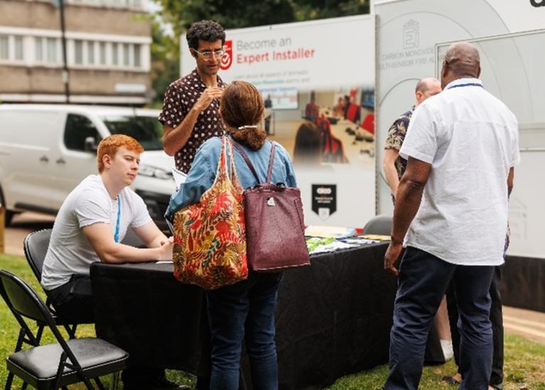 A man and a woman gather around a pop-up table outside where volunteers wearing lanyards answer questions.