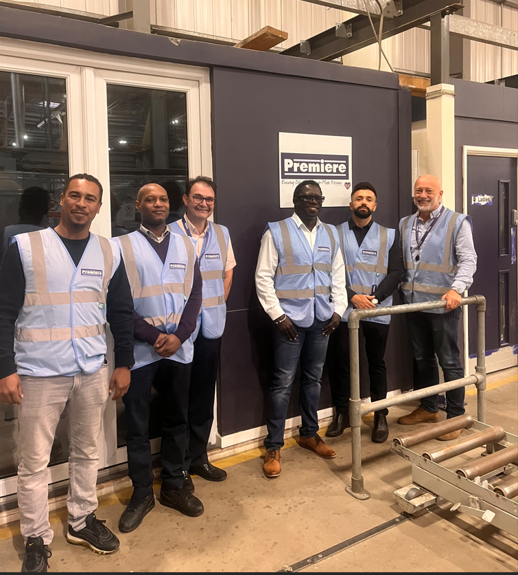 6 men standing in front of cabin with premiere kitchen logo wearing blue high vis vests
