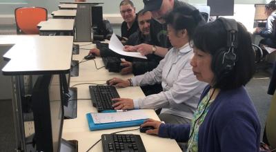 A male member of Library staff helping a mixed group of Library users on PC's