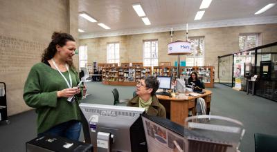 A female member of the libraries and archives team having a conversation with a female library customer.