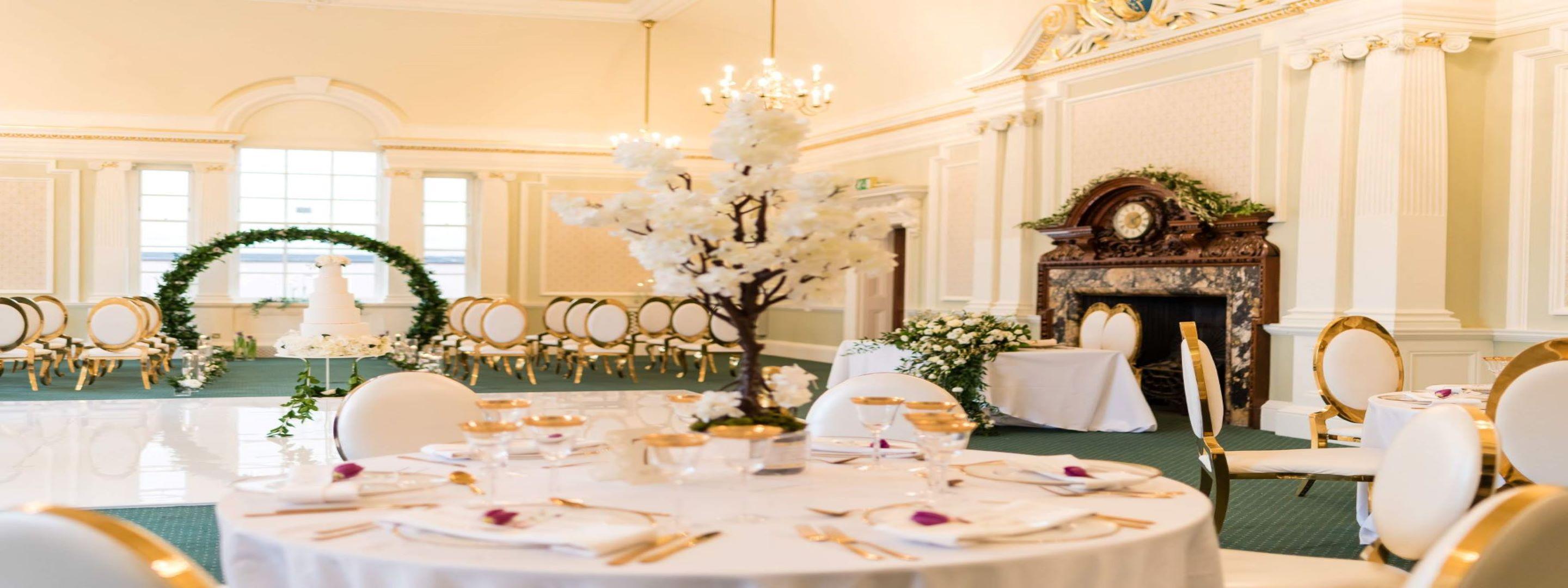 Grand room set up for and event with chair and tables laid out with cutlery and decorations.